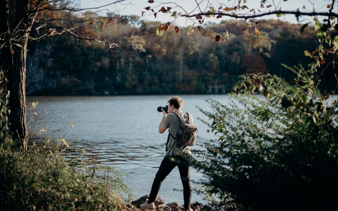 man holding a camera, view across lake
