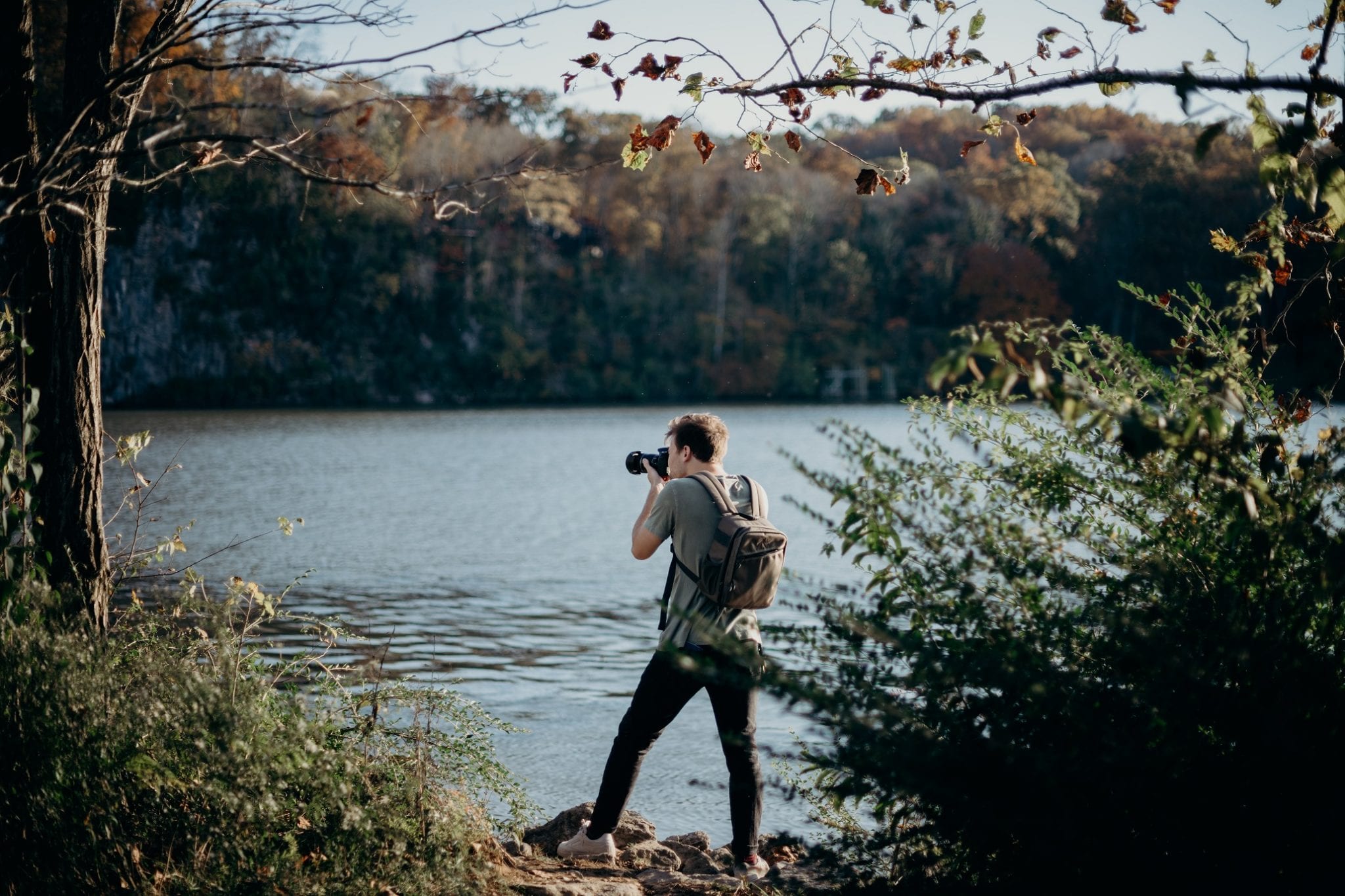 man holding a camera, view across lake